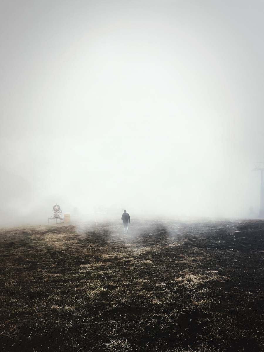 fog man in black jacket walking on brown field with mist at daytime weather