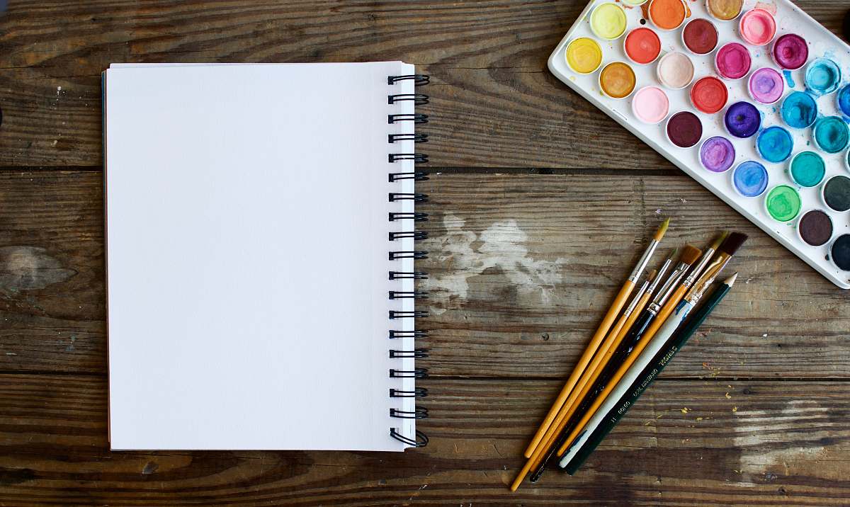 creative paint brushes next to drawing book and water color palette craft