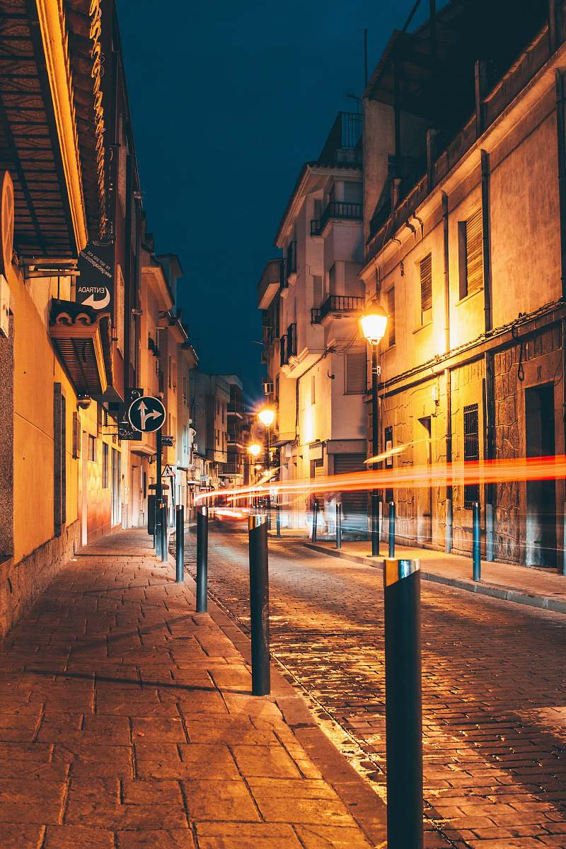town time-lapse photography of vehicle passing on the road between street lights and buildings during night time pavement