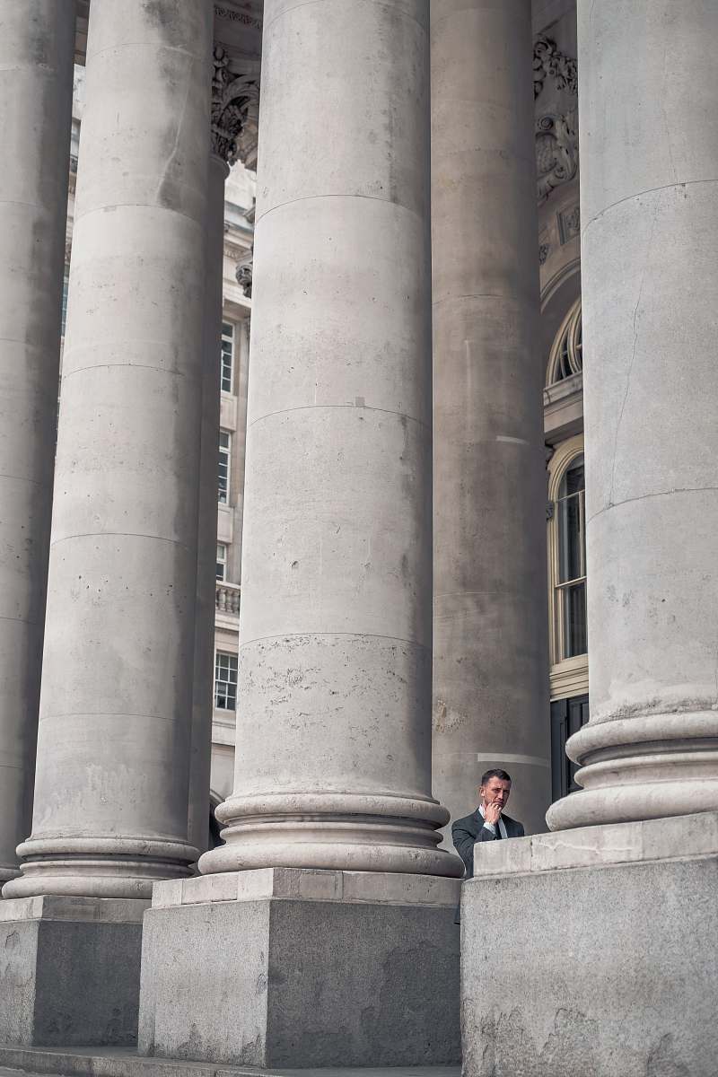 pillar man standing beside gray concrete pillars grey