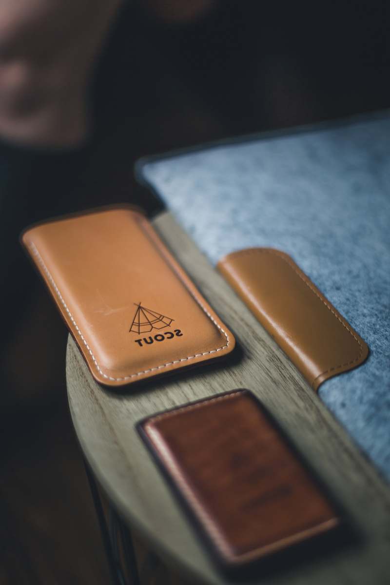 brown Leather laptop cover, wallet, and phone holder with a label that reads "SCOUT" on a wooden circular table phone case