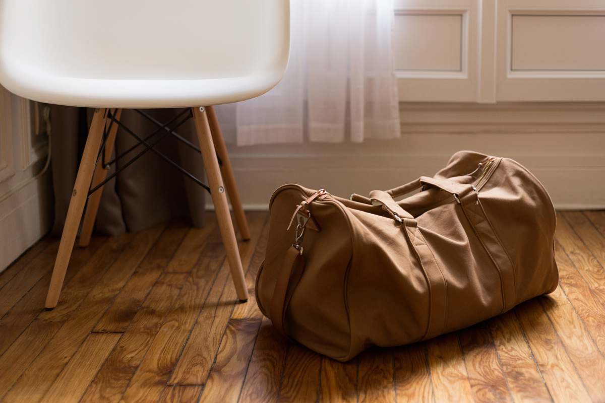 bag brown duffel bag beside white and brown wooden chair wood