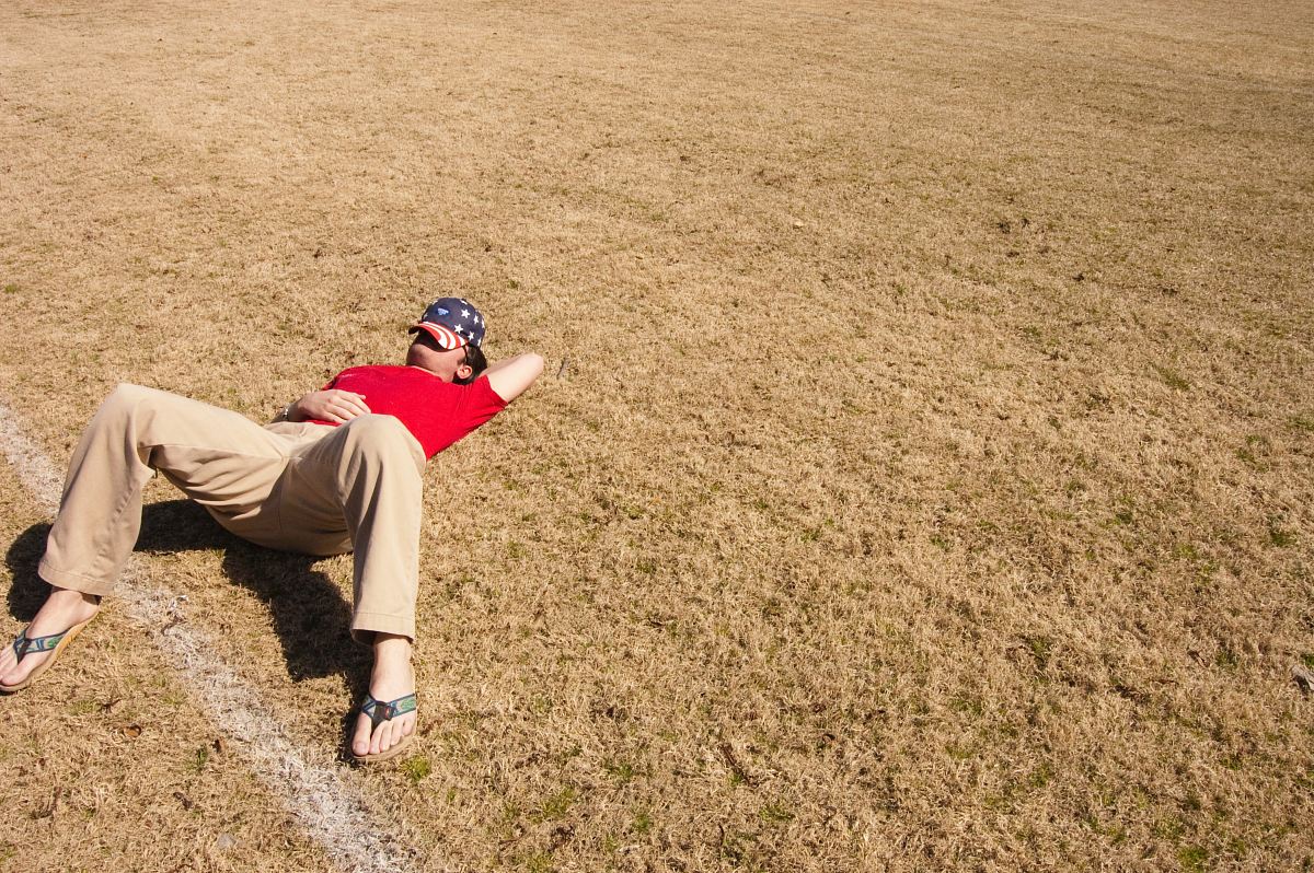 man in red top lying on lawn field during daytime
