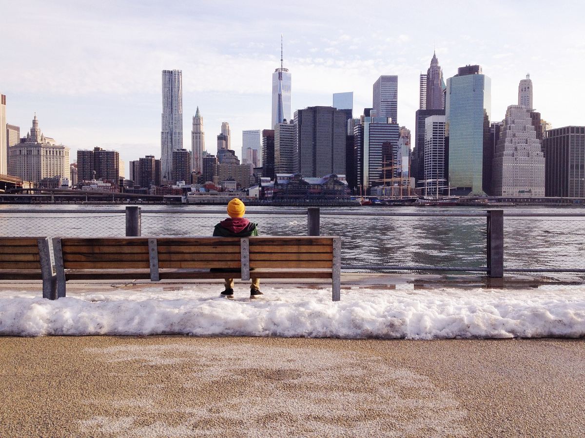 person in knit cap sitting on wooden bench in front of body of water during daytime
