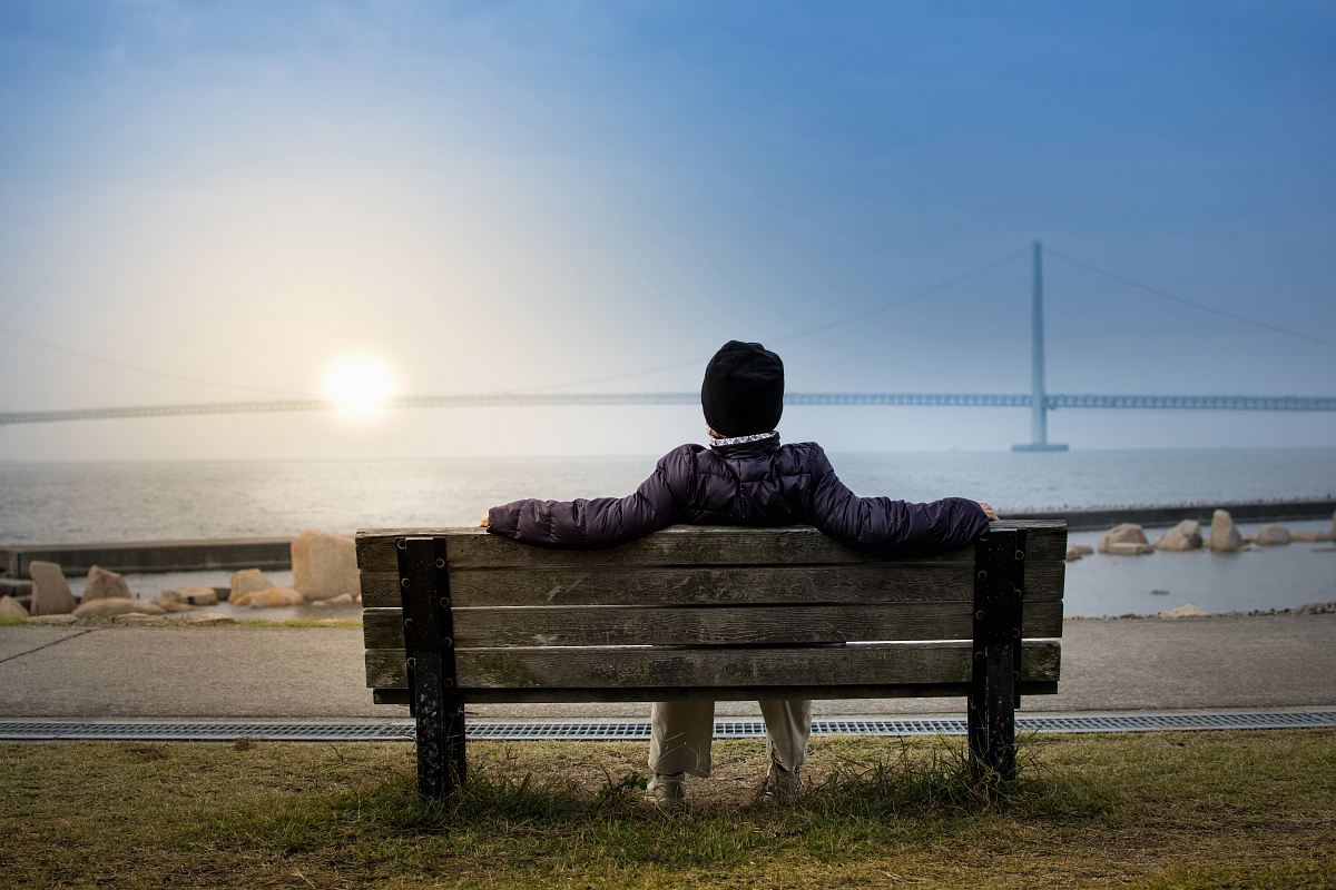 person sitting on bench facing suspension bridge