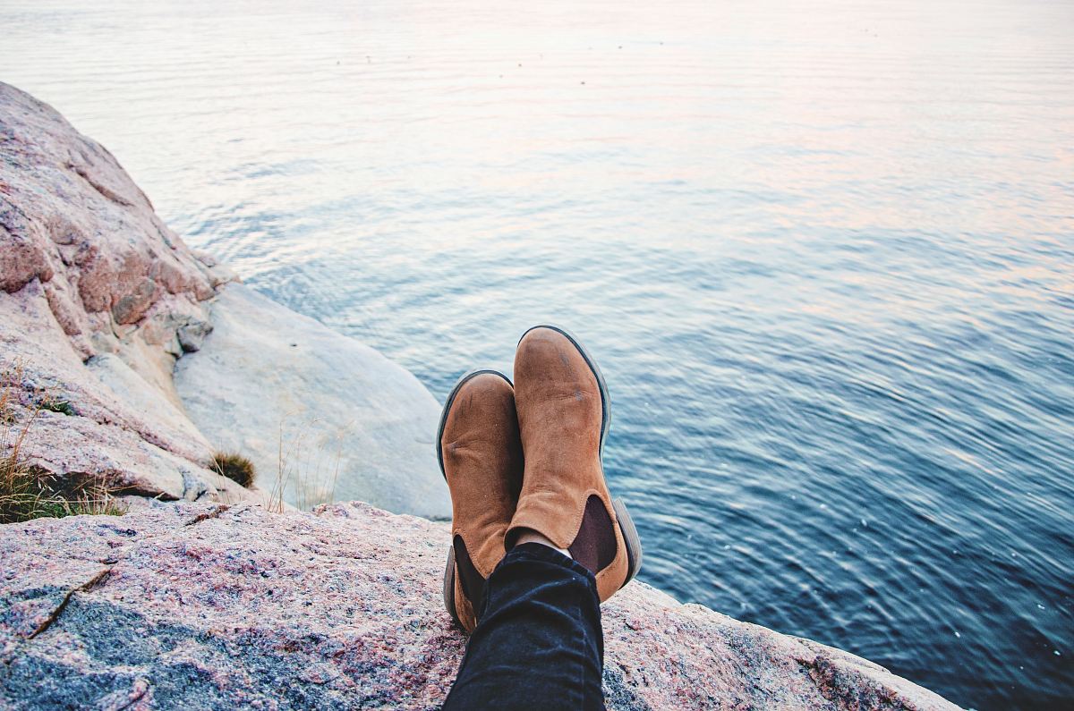 person sitting on gray rock beside body of water during daytime