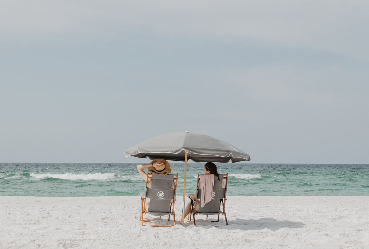 two people under beach umbrella near shoreline