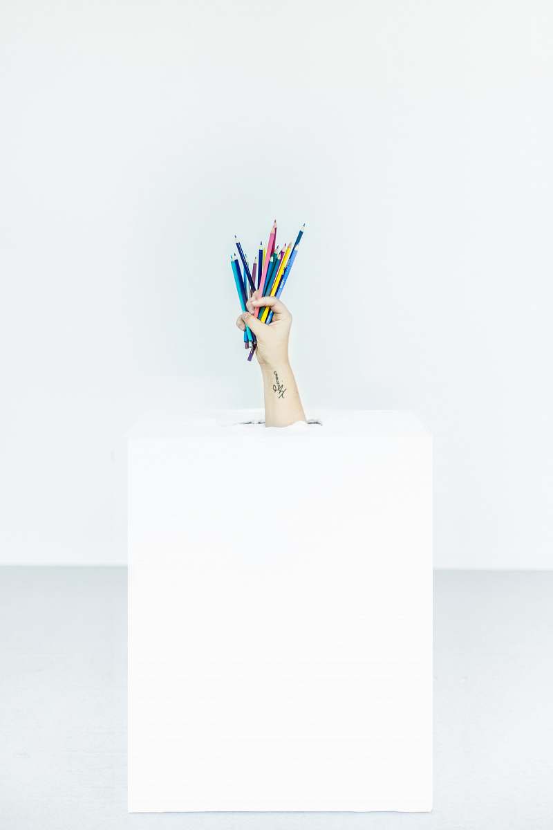 pencils person's hand burst out of box holding assorted-color pens hand