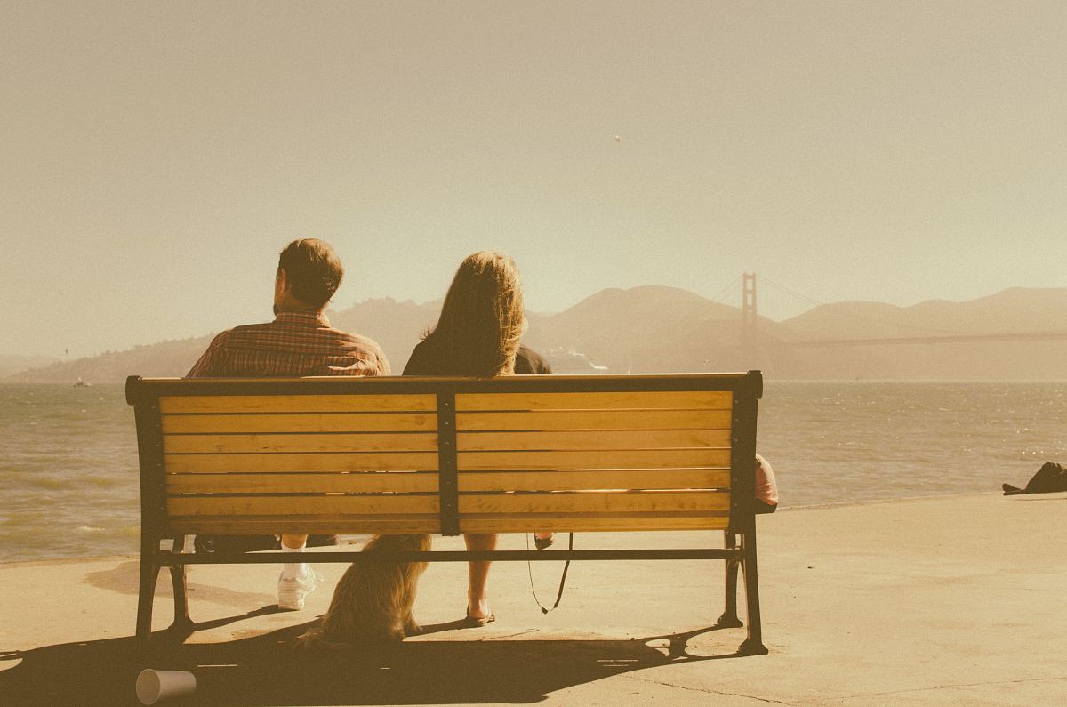 man and woman sitting on bench beside body of water
