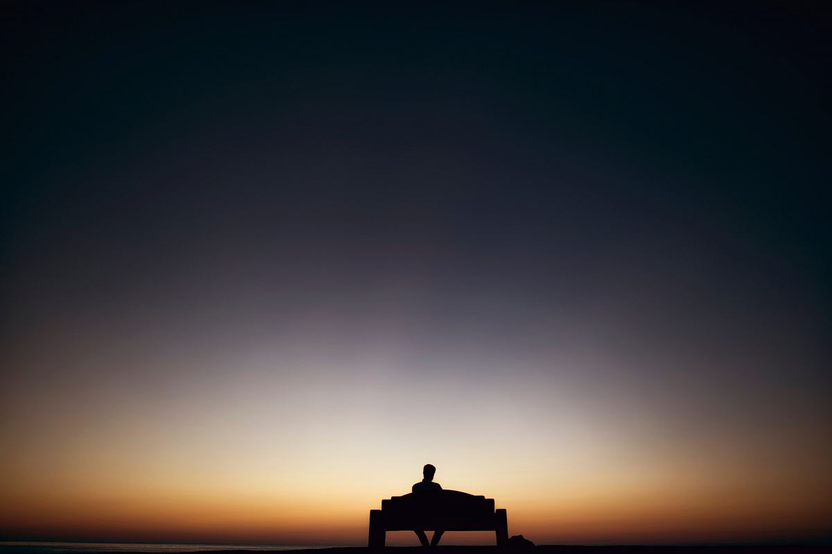 man sitting on bench facing sunset