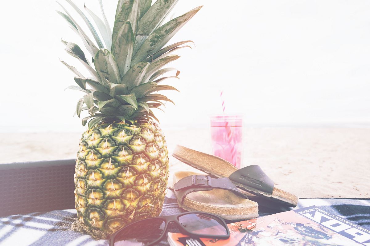 minimalist photography of pineapple near sandals and sunglasses