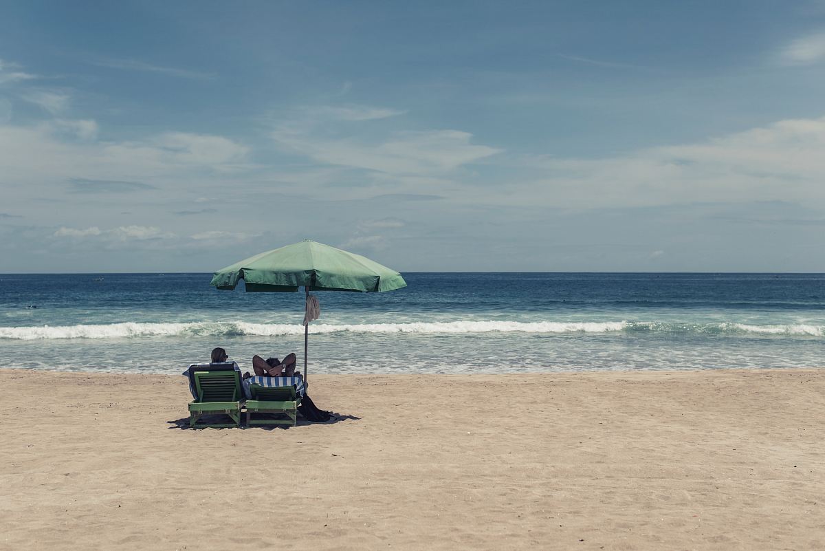people sitting on seashore under green umbrella during daytime