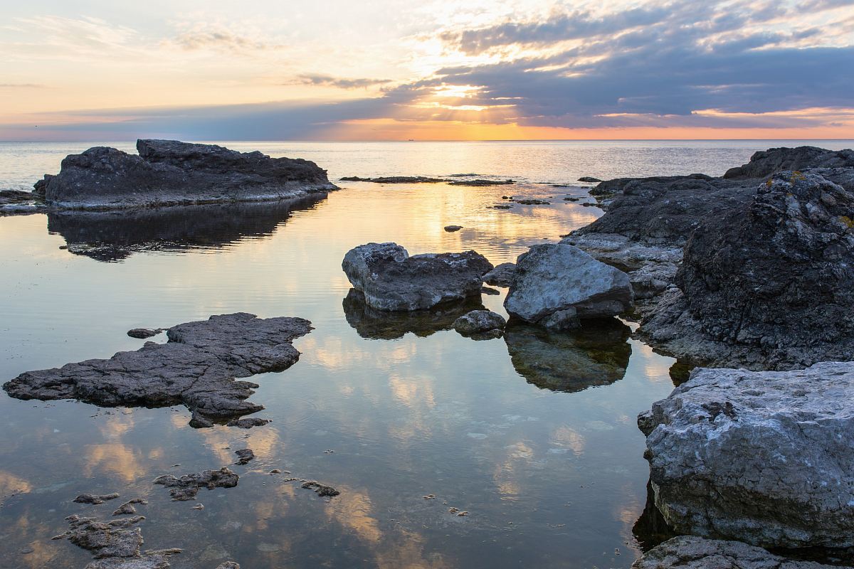 rocks on body of water under cloudy sky