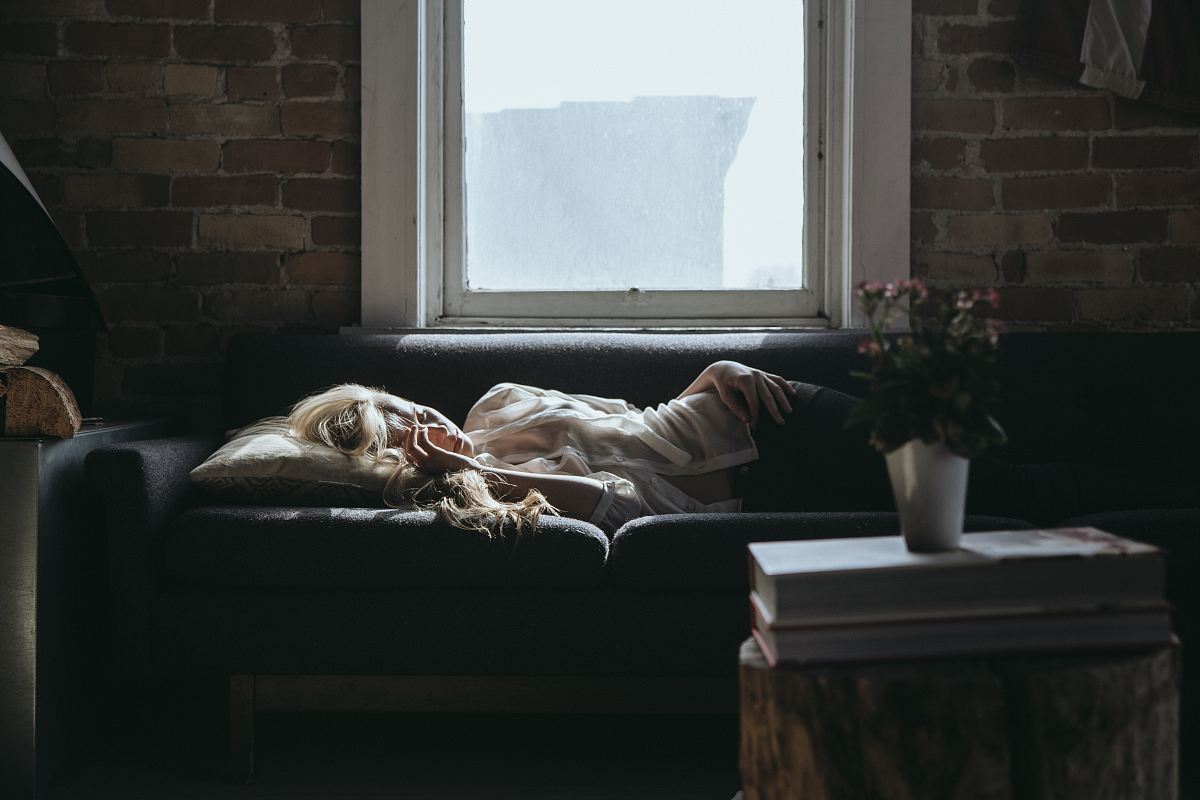 woman lying on sofa near closed window during daytime