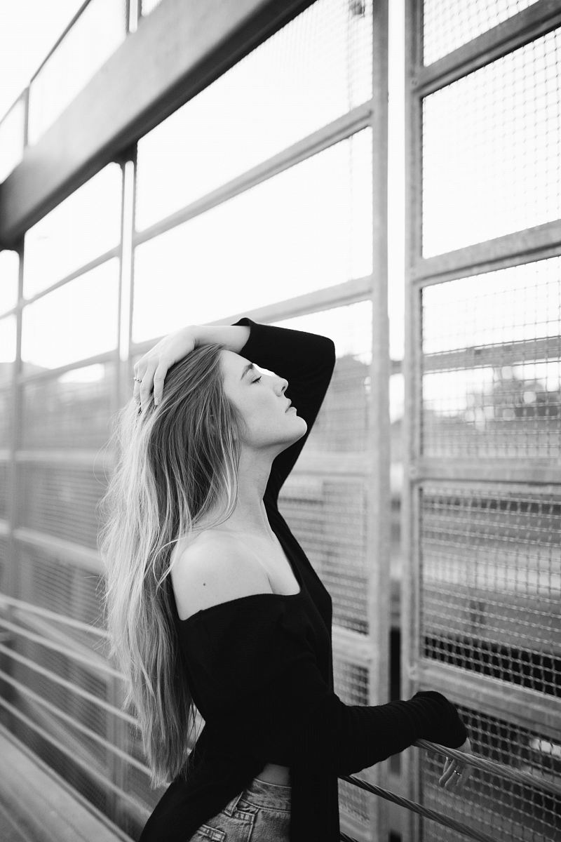 woman wearing off-shoulder top posing beside steel gate in grayscale photography