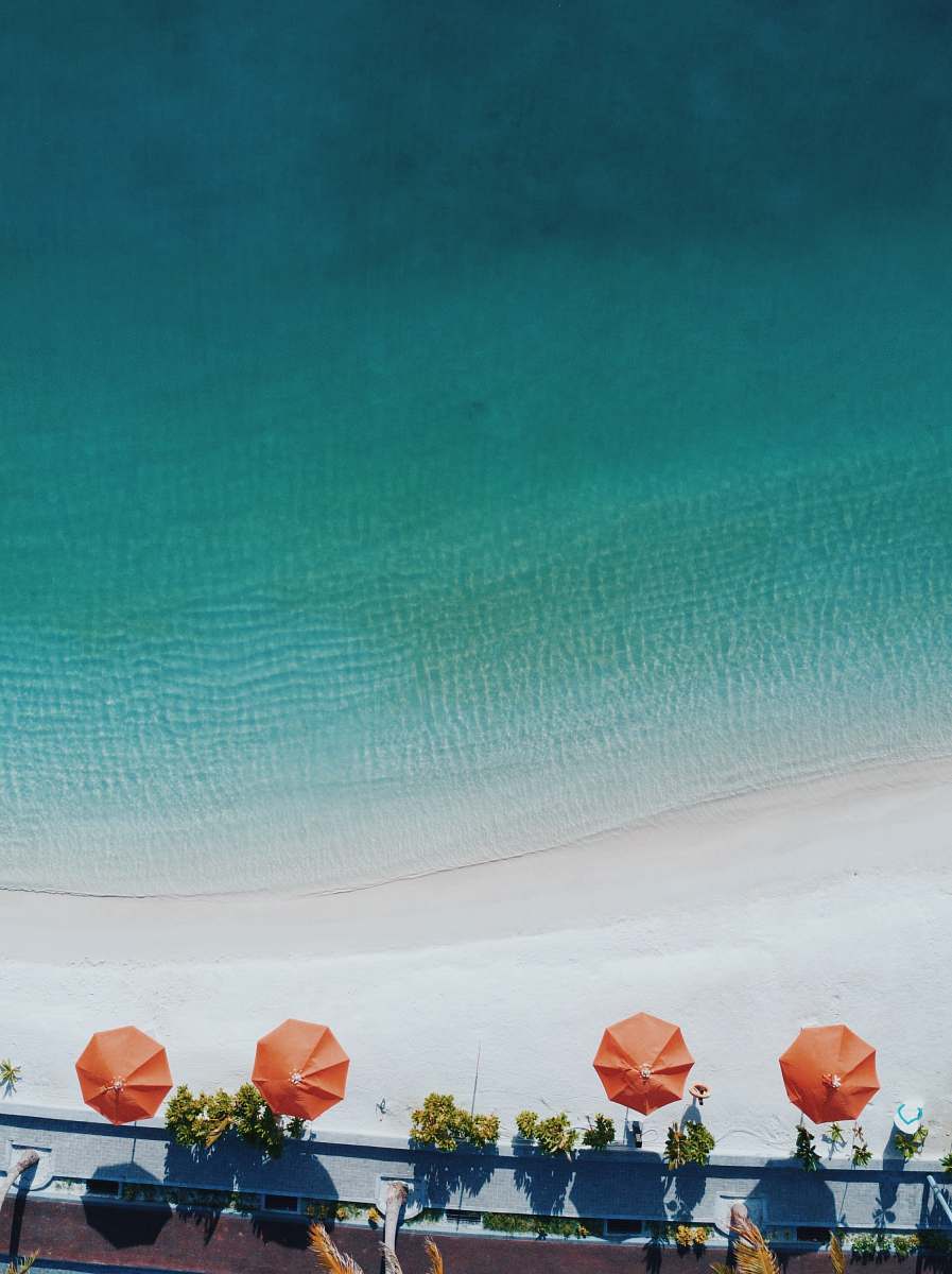 umbrella aerial photography of four orange patio umbrellas on seashore canopy