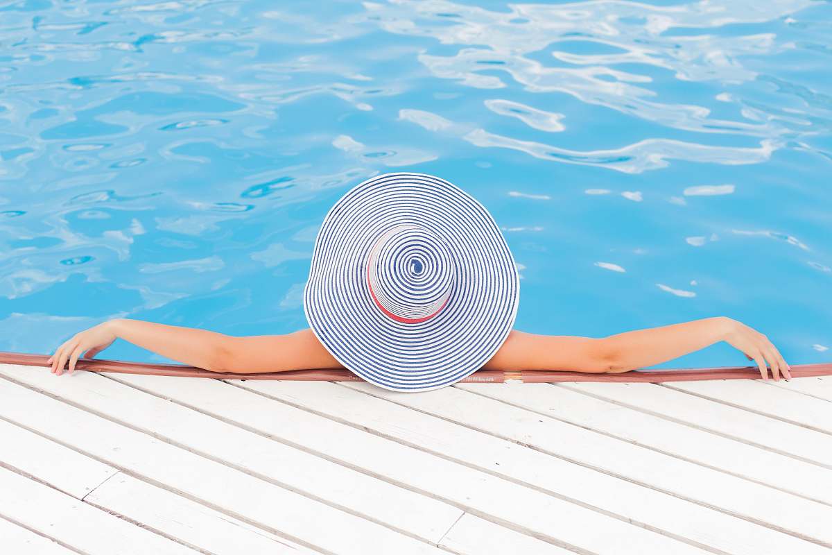 woman woman leaning on white concrete surface beside swimming pool during daytime pool