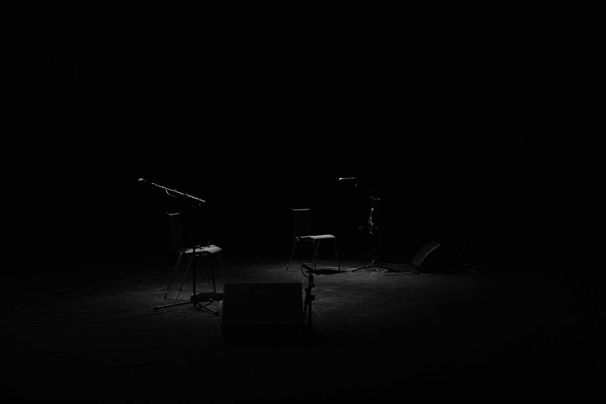 black-and-white A dim shot of two chairs and microphone stands on an empty stage music