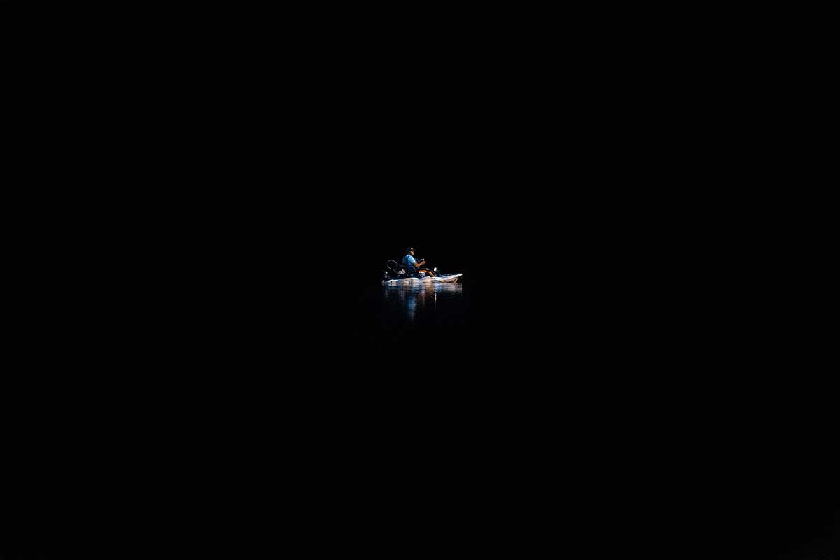boat A person on a canoe in the water surrounded by complete darkness. background