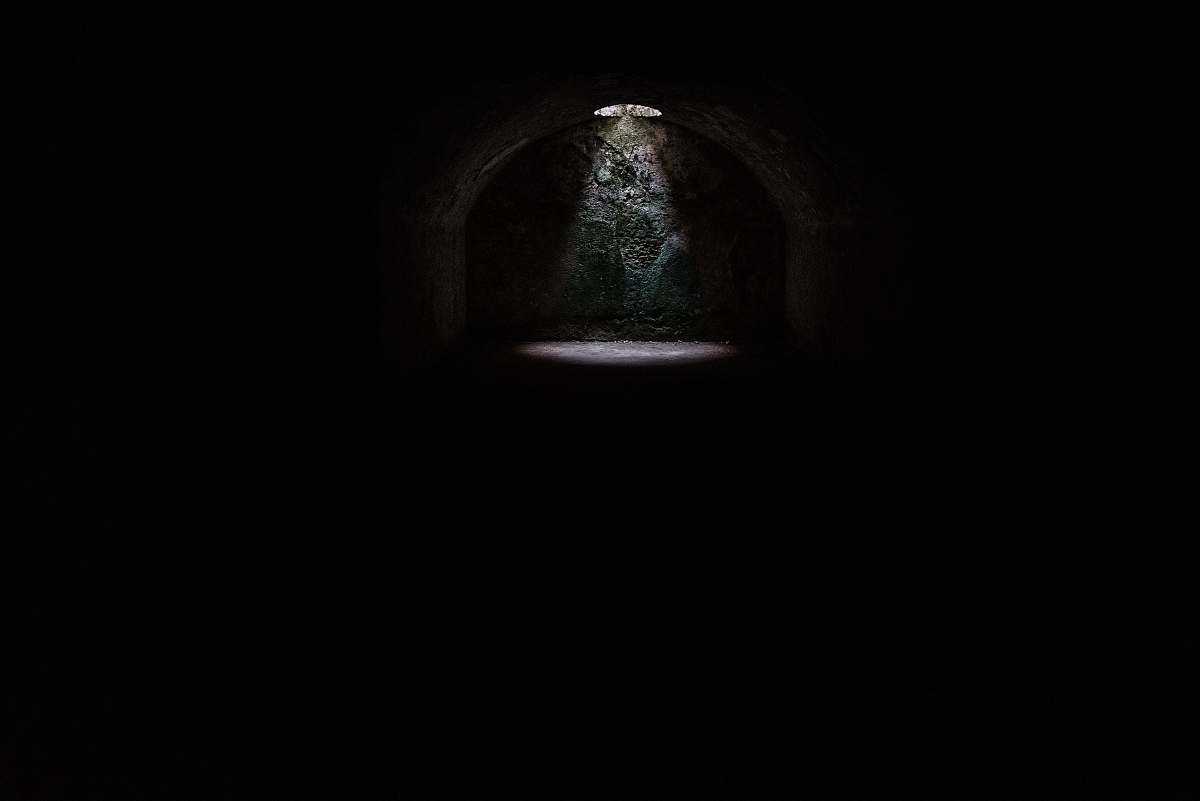 black-and-white A spotlight coming from a hole in a dark underground cave in Minorca dark
