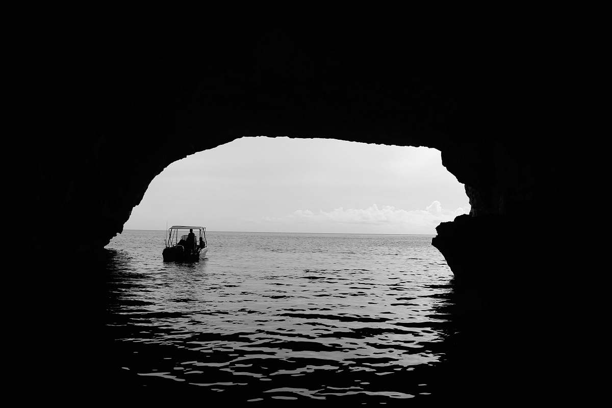 arch boat on body of water outside the cave grey
