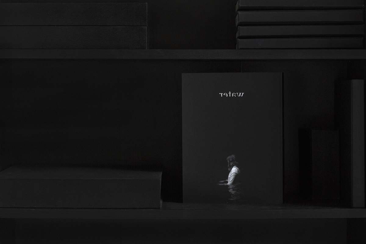 black Shelf with books that is dark except for "water" magazine with a person wading on cover book