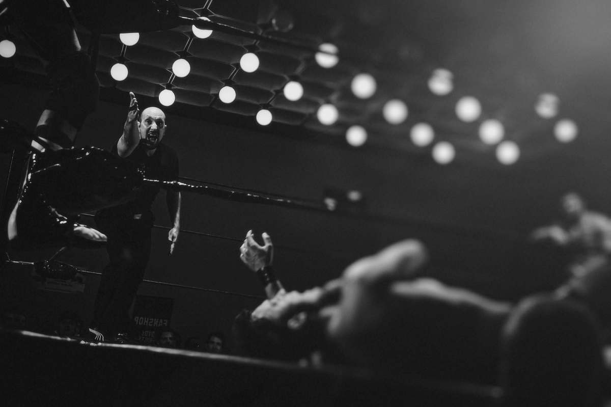 Experience the energy of a unique boxing match set in the vibrant city of Prague, featuring two men passionately engaged in the sport. One of the fighters, dressed in a sharp black suit and tie, stands confidently on stage, embodying the fusion of elegance and athleticism. This captivating scene is perfect for illustrating themes of competition, urban culture, and the unexpected intersection of formal attire and sports, making it suitable for advertising, editorial content, or creative projects.