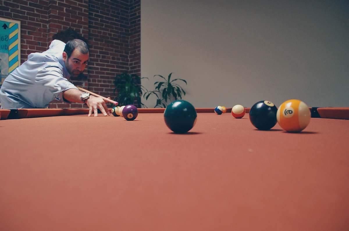 person man playing billiard near green leafed plants people