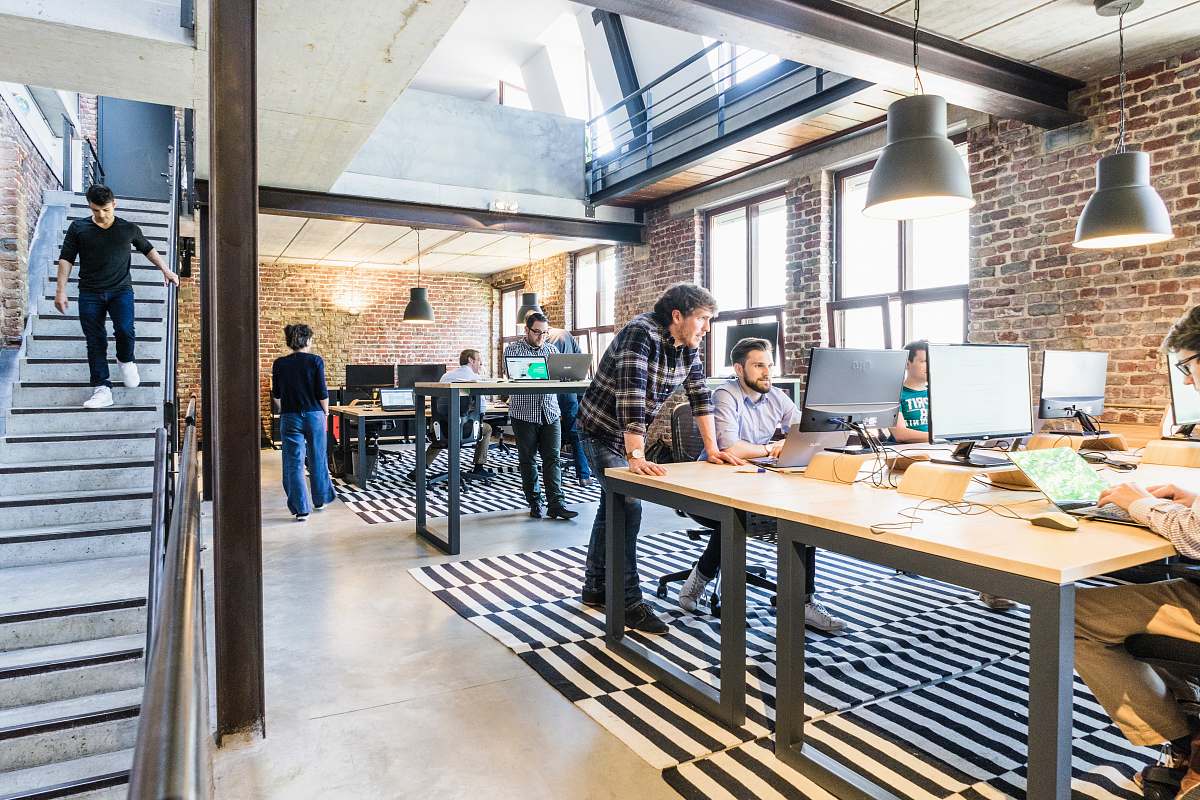 person man standing beside another sitting man using computer furniture