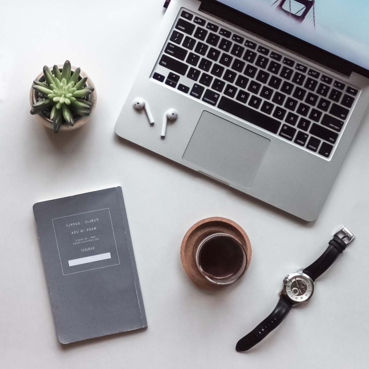 jewelry flat-lay photography of MacBook, coffee-filled cup, book, and wristwatch brooch