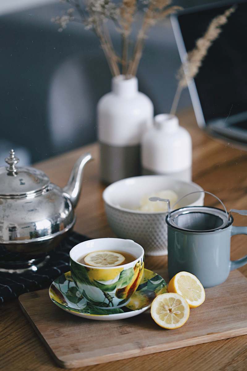saucer gray teapot beside mug filled with tea and lemon on top of table tea