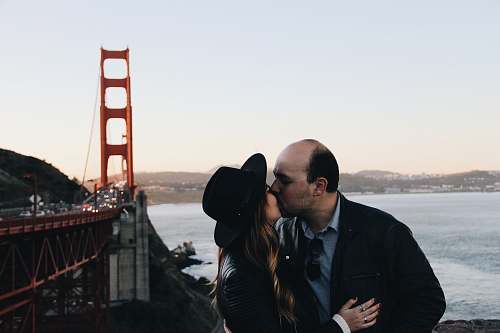 person man and woman kissing beside Golden Gate Bridge during daytime people