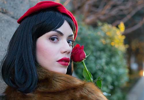 person woman wearing brown coat holding red rose near wall during daytime people