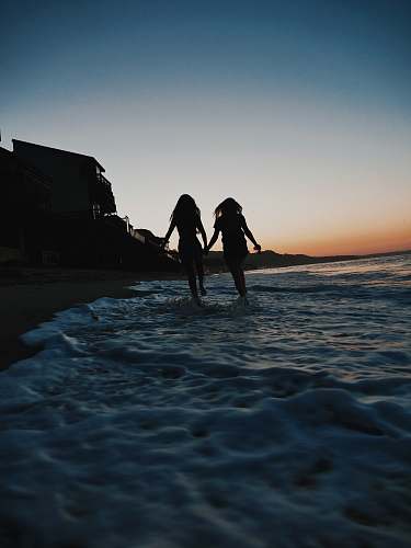 coast silhouette of two women running across seashore beach