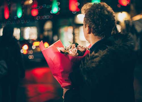 human man in black faux fur coat holding bouquet of floweers people