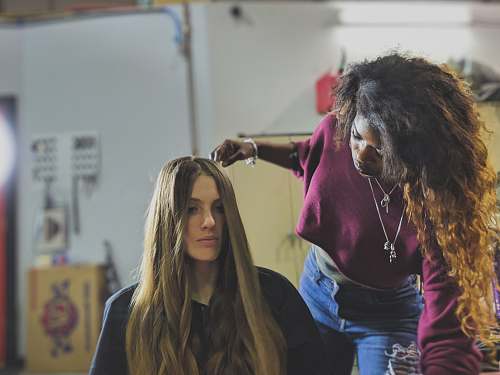 human woman arranging the hair of woman sitting on chair apparel
