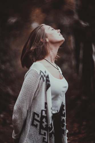 human standing woman in white scoop-neck tank top with beige cardigan with her eyes close in selective focus photography person