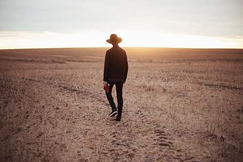 people man walking on dried plain while looking towards the sun on horizon human