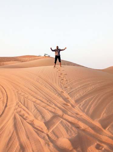 outdoors man standing on brown desert during daytime soil