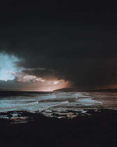 beach body of water under dark clouds ocean