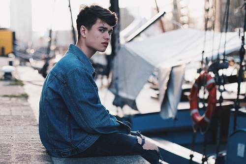 person man in blue denim jacket sitting on dock human
