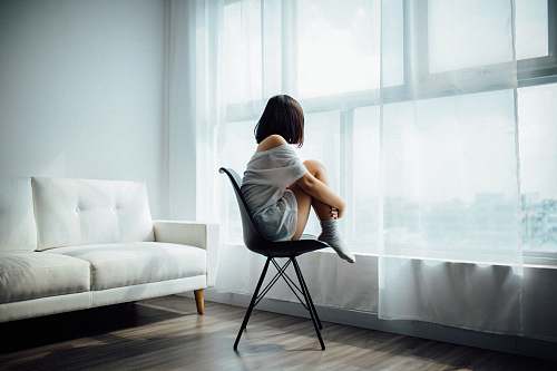 chair woman sitting on black chair in front of glass-panel window with white curtains furniture