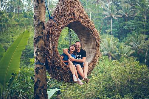human man and woman riding on brown hammock beside brown tree people