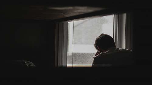 grey man looking outside by window window