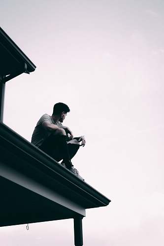 person grayscale photography of man sitting on dock banister