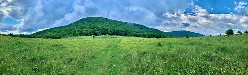 outdoors green grass field near green mountain under white clouds and blue sky during daytime field