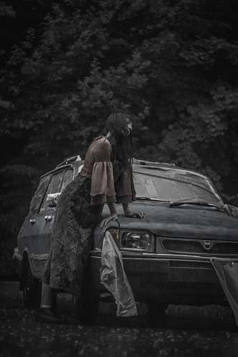 car greyscale photography of woman beside vehicle automobile