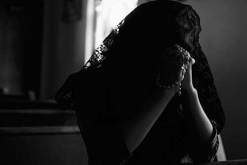 person grayscale photography of woman praying while holding prayer beads black-and-white