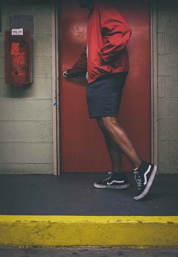 person man wearing red jacket holding door knob near red wooden door people