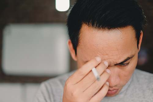 people person holding cigarette stick and scratching his face person